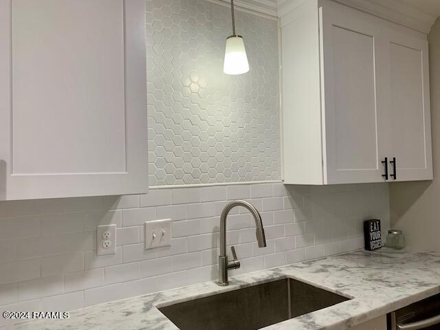 kitchen featuring light stone counters, backsplash, a sink, and white cabinets