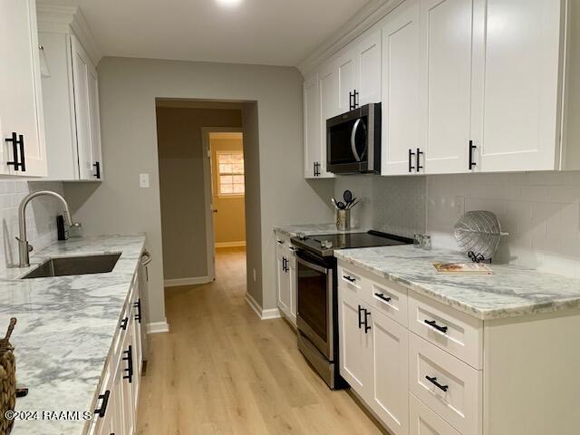 kitchen with appliances with stainless steel finishes, light wood-style floors, white cabinets, a sink, and light stone countertops