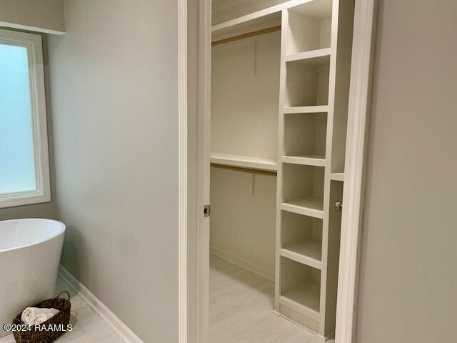 full bathroom featuring a freestanding bath, a spacious closet, and baseboards