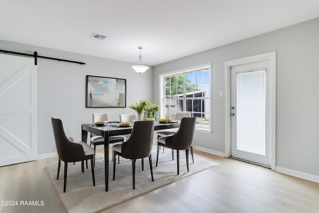 dining room featuring light wood finished floors, a barn door, visible vents, and baseboards