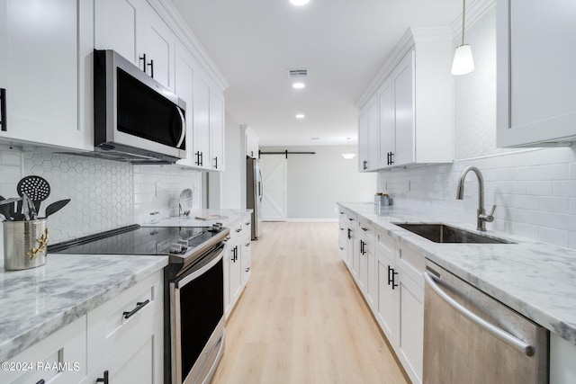 kitchen featuring a barn door, stainless steel appliances, a sink, white cabinets, and light wood finished floors