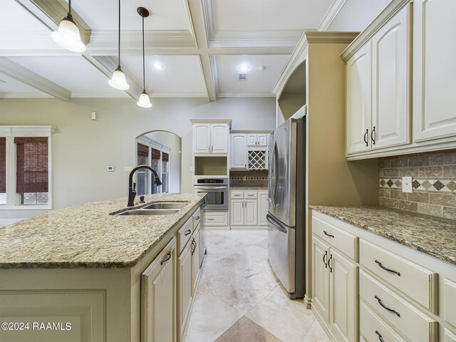 kitchen with sink, light stone counters, decorative light fixtures, a center island with sink, and appliances with stainless steel finishes