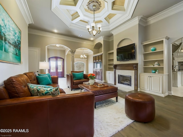 living room with ornate columns, a tile fireplace, wood-type flooring, crown molding, and an inviting chandelier