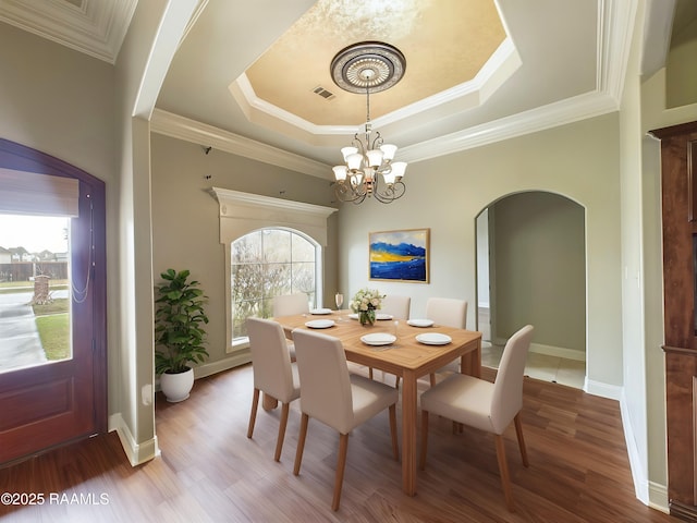 dining room with an inviting chandelier, ornamental molding, a tray ceiling, and hardwood / wood-style floors