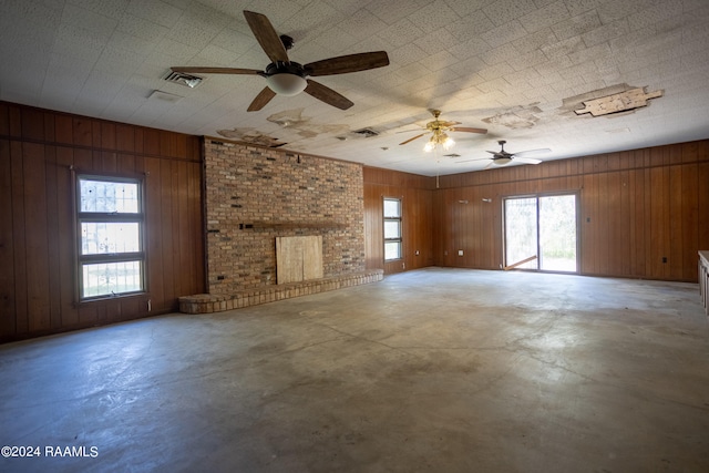 unfurnished living room with brick wall, wood walls, ceiling fan, and a fireplace