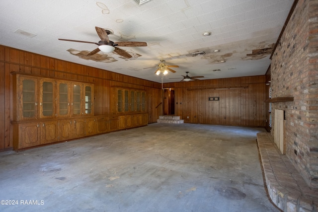 interior space with ceiling fan, wood walls, brick wall, and a large fireplace