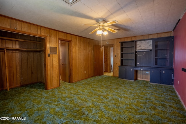 interior space with dark colored carpet, wooden walls, and ceiling fan