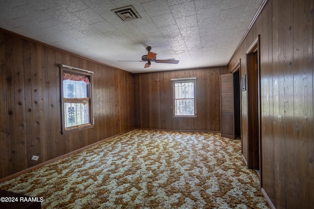 spare room with ceiling fan, wood walls, and carpet