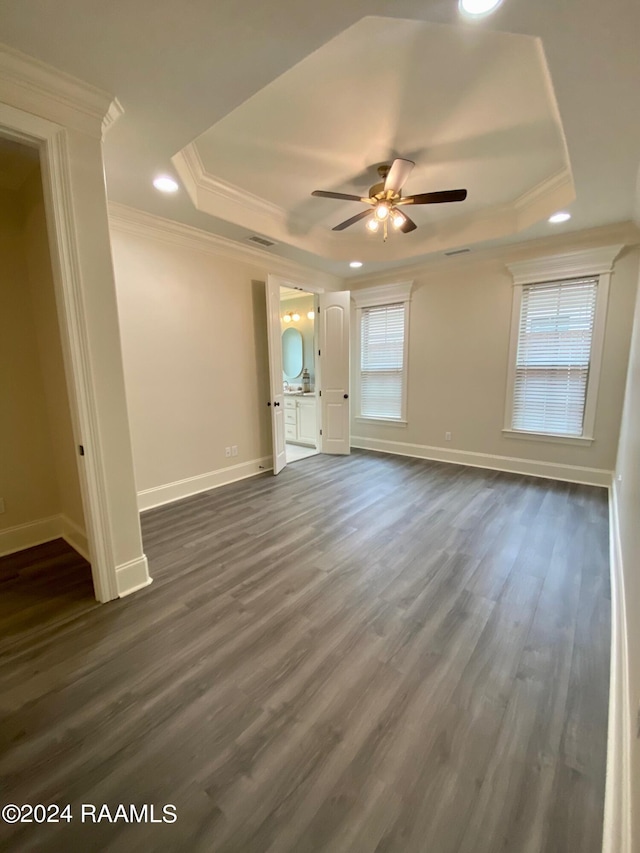 interior space with a tray ceiling, ceiling fan, dark wood-type flooring, and ornamental molding