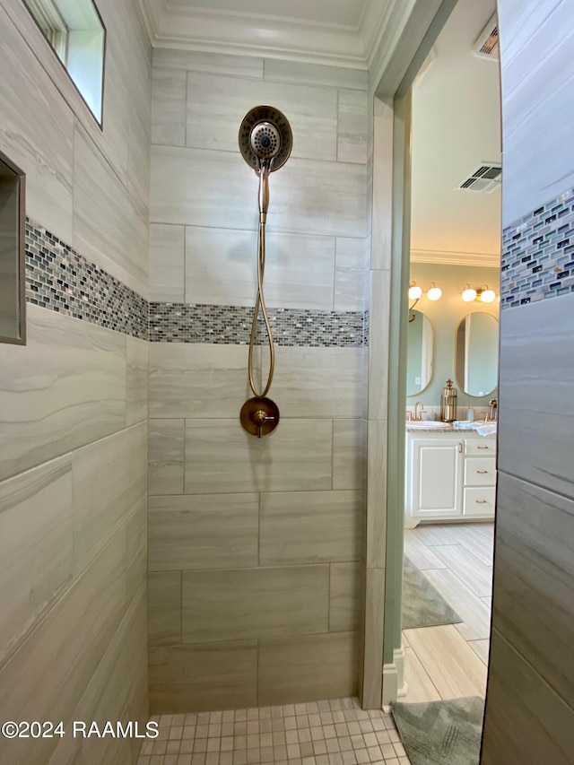 bathroom with tiled shower, ornamental molding, and vanity