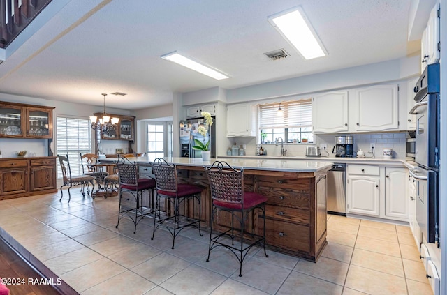 kitchen featuring light tile flooring, an inviting chandelier, decorative light fixtures, a kitchen breakfast bar, and white cabinets