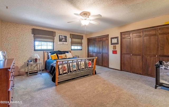 carpeted bedroom with multiple closets, ceiling fan, and a textured ceiling