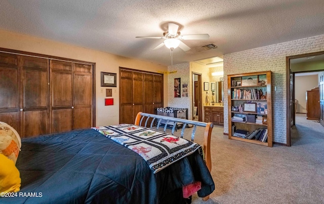 bedroom featuring ceiling fan, a textured ceiling, light colored carpet, brick wall, and two closets