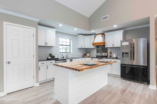 kitchen featuring custom range hood, stainless steel appliances, tasteful backsplash, and white cabinetry