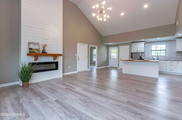 unfurnished living room with an inviting chandelier, sink, light wood-type flooring, and high vaulted ceiling