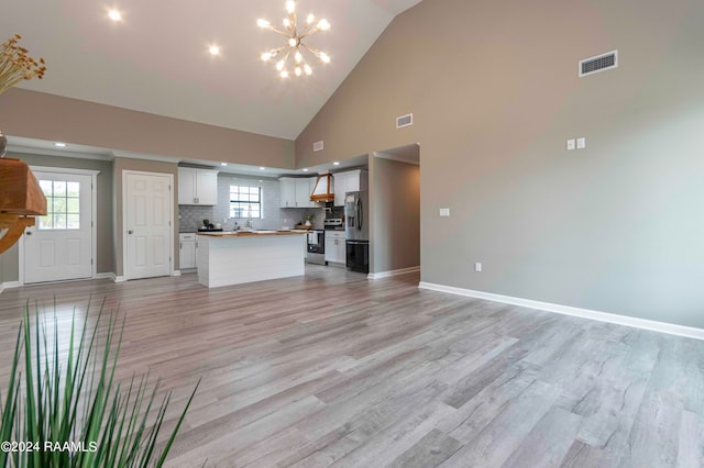 unfurnished living room with high vaulted ceiling, an inviting chandelier, light hardwood / wood-style floors, and sink