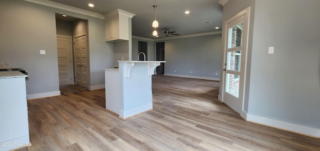 kitchen featuring light hardwood / wood-style flooring, ceiling fan, pendant lighting, ornamental molding, and a breakfast bar