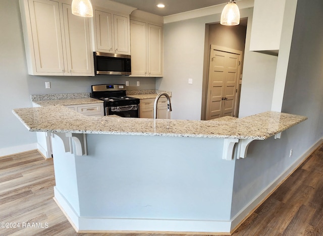 kitchen featuring a kitchen breakfast bar, decorative light fixtures, appliances with stainless steel finishes, and hardwood / wood-style flooring