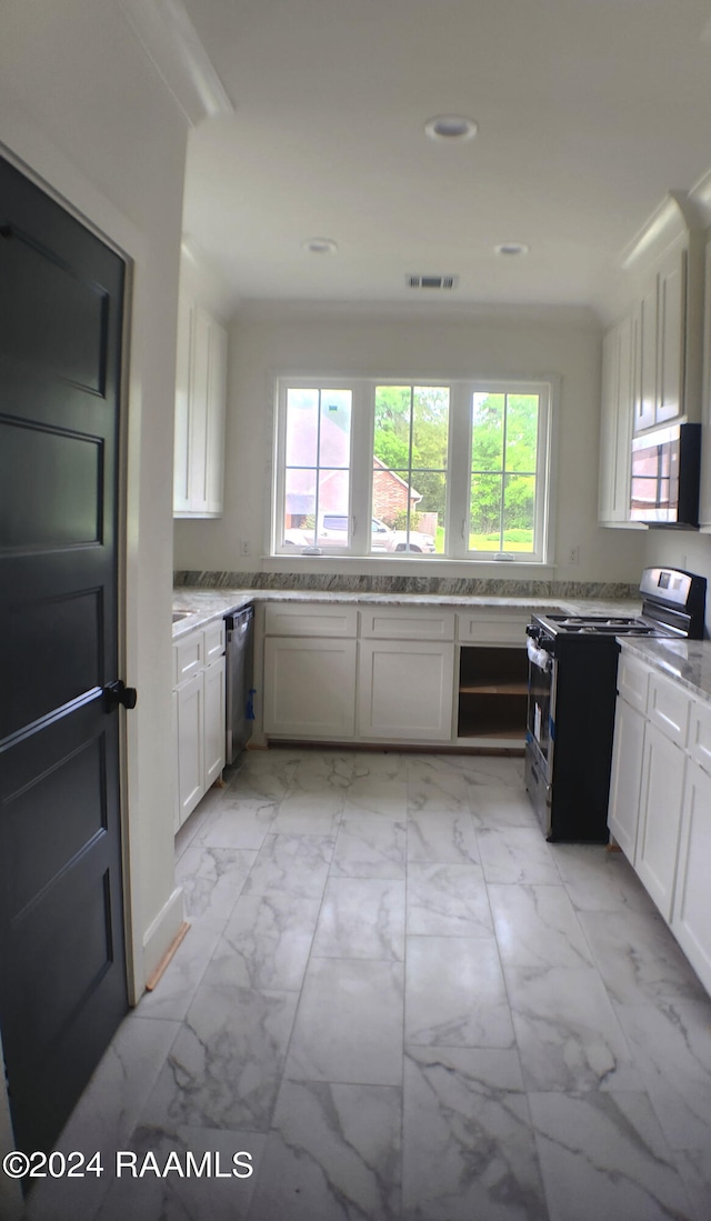 kitchen with appliances with stainless steel finishes, a wealth of natural light, light stone counters, and white cabinetry