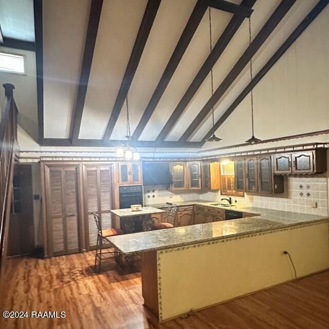 kitchen with sink, vaulted ceiling with beams, kitchen peninsula, black oven, and light wood-type flooring