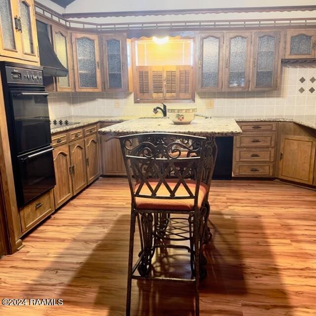 kitchen featuring tasteful backsplash, light stone counters, black appliances, light hardwood / wood-style floors, and range hood