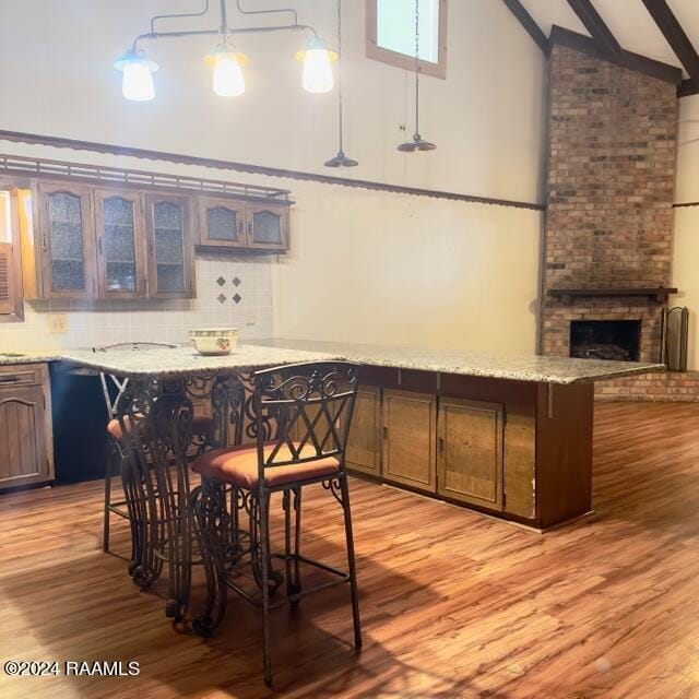 bar featuring a brick fireplace, beam ceiling, decorative light fixtures, high vaulted ceiling, and light hardwood / wood-style flooring