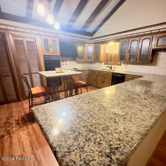 kitchen featuring kitchen peninsula, hardwood / wood-style floors, black appliances, and vaulted ceiling