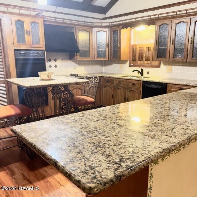 kitchen featuring light stone countertops, hardwood / wood-style floors, a breakfast bar area, decorative backsplash, and black appliances