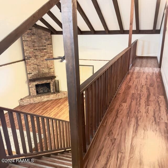 staircase featuring hardwood / wood-style flooring, lofted ceiling with beams, and a fireplace