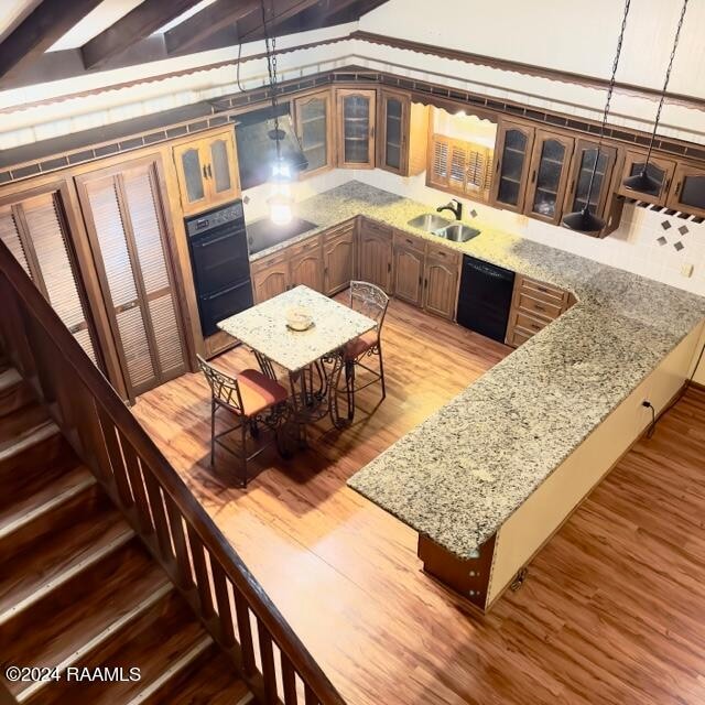 interior space featuring sink, black appliances, wood-type flooring, stone countertops, and beamed ceiling