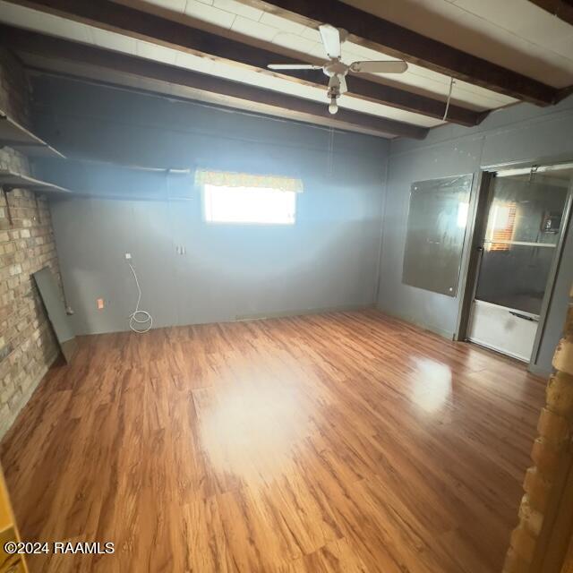 spare room with ceiling fan, beam ceiling, wood-type flooring, and a brick fireplace