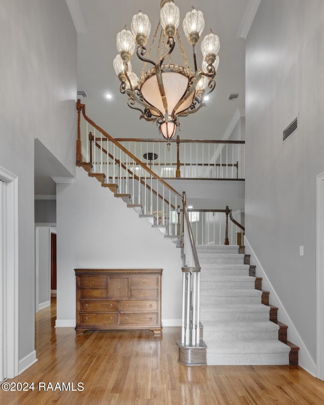 stairway featuring crown molding, a high ceiling, hardwood / wood-style flooring, and an inviting chandelier