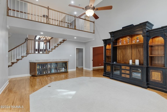 living room featuring light hardwood / wood-style flooring, ceiling fan with notable chandelier, and a towering ceiling