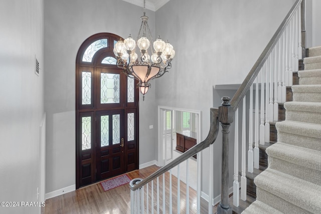 foyer entrance featuring a towering ceiling, ornamental molding, a notable chandelier, and dark hardwood / wood-style floors