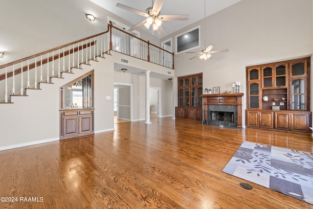 unfurnished living room with a high end fireplace, a towering ceiling, decorative columns, ceiling fan, and hardwood / wood-style floors