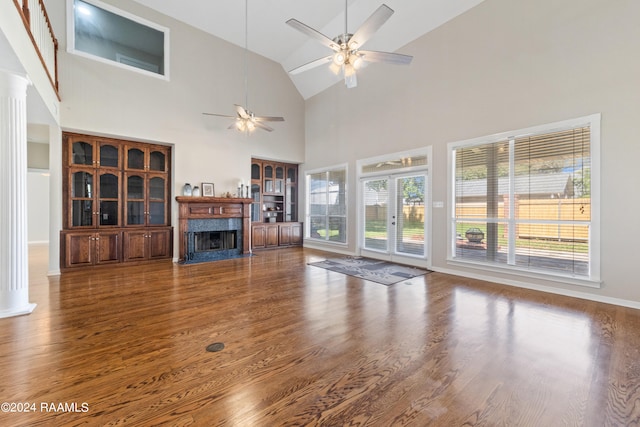 unfurnished living room with decorative columns, ceiling fan, dark wood-type flooring, high vaulted ceiling, and a premium fireplace