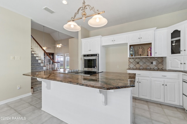 kitchen featuring dark stone counters, white cabinets, oven, hanging light fixtures, and ceiling fan