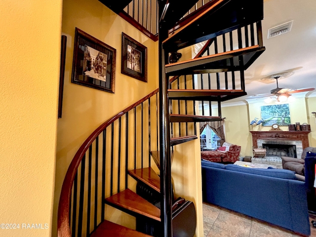 staircase featuring light tile flooring, a brick fireplace, ceiling fan, and crown molding