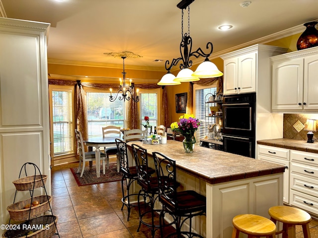 kitchen with black double oven, backsplash, a kitchen bar, decorative light fixtures, and a chandelier