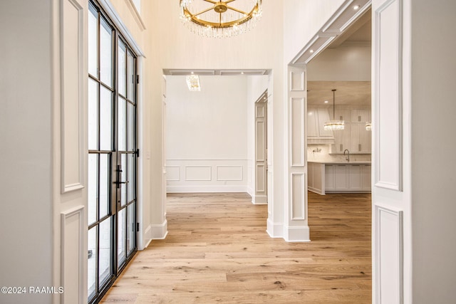 hall featuring a towering ceiling, a chandelier, sink, and light wood-type flooring