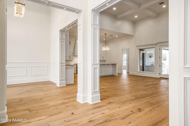 unfurnished living room with beamed ceiling, a towering ceiling, light hardwood / wood-style flooring, crown molding, and coffered ceiling