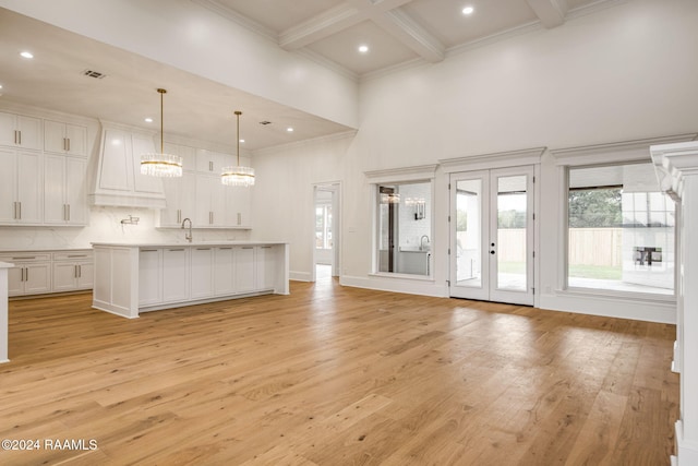 unfurnished living room with light hardwood / wood-style floors, beam ceiling, sink, and a towering ceiling