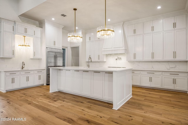 kitchen featuring stainless steel built in fridge, a center island with sink, white cabinetry, pendant lighting, and light hardwood / wood-style flooring