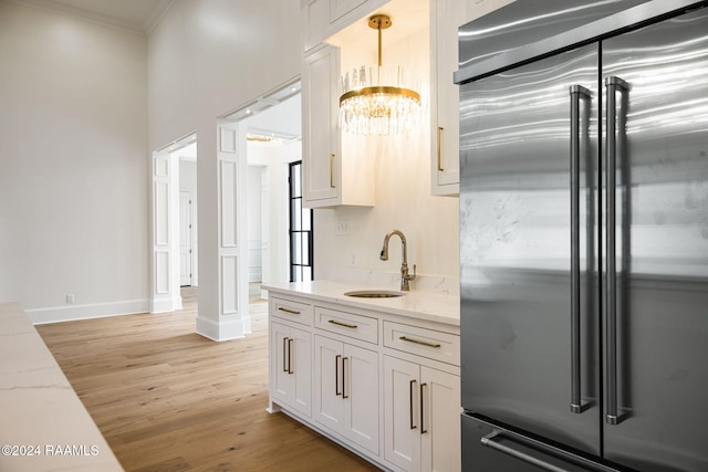 kitchen with light stone counters, sink, ornamental molding, white cabinetry, and high quality fridge