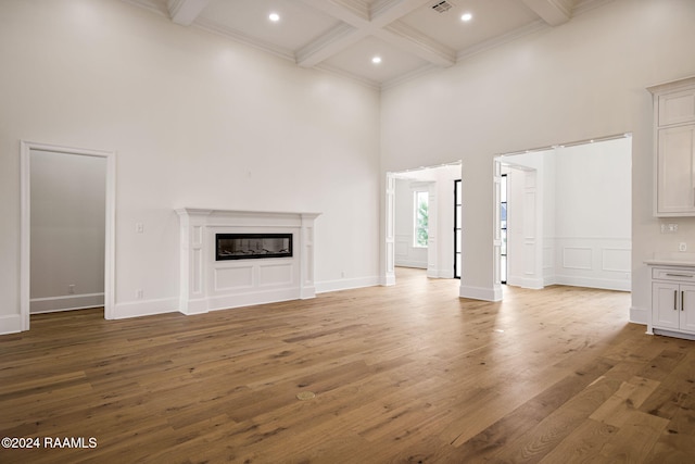 unfurnished living room with hardwood / wood-style floors, a high ceiling, beam ceiling, and ornamental molding