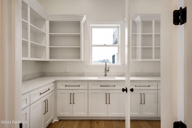 kitchen with hardwood / wood-style flooring, white cabinetry, sink, and light stone counters