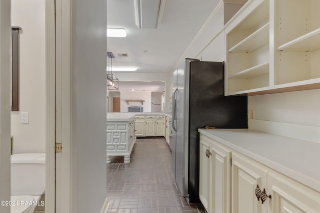 kitchen featuring stainless steel refrigerator, ornamental molding, and white cabinets