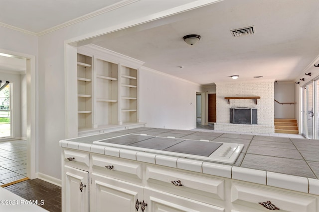 kitchen with tile counters, a fireplace, brick wall, and white cabinetry