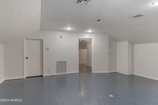 additional living space with brick wall, dark wood-type flooring, and vaulted ceiling