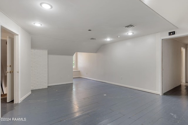 empty room with brick wall, dark wood-type flooring, and lofted ceiling